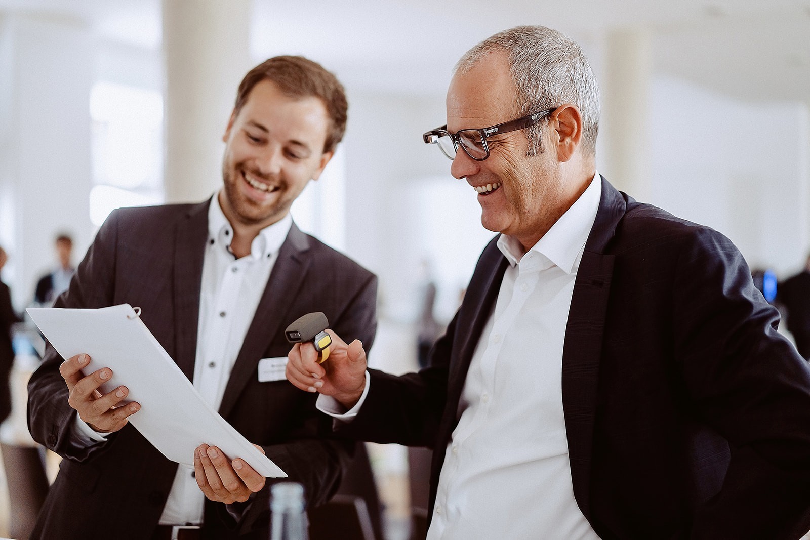 Zwei lachende Männer schauen auf ein Blatt Papier und testen Pick-by-Vision 