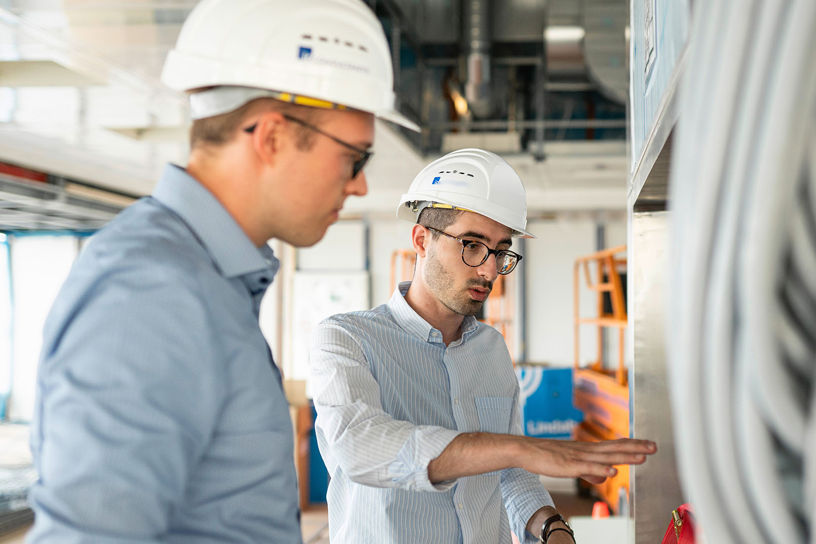 Two men wearing construction helmets discuss a problem on site