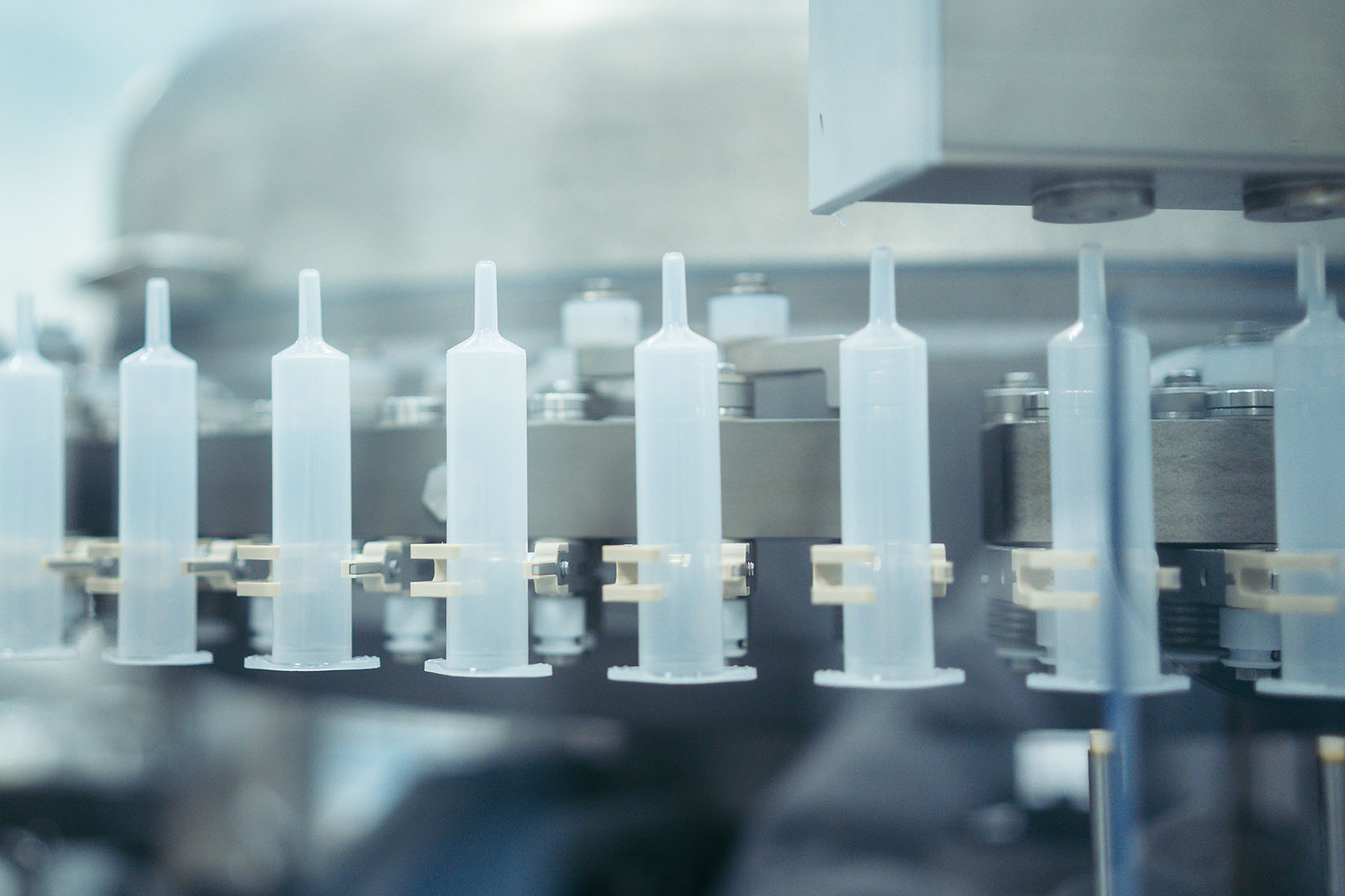 A close-up view of a series of transparent syringes lined up on a production line, showcasing precision in manufacturing.