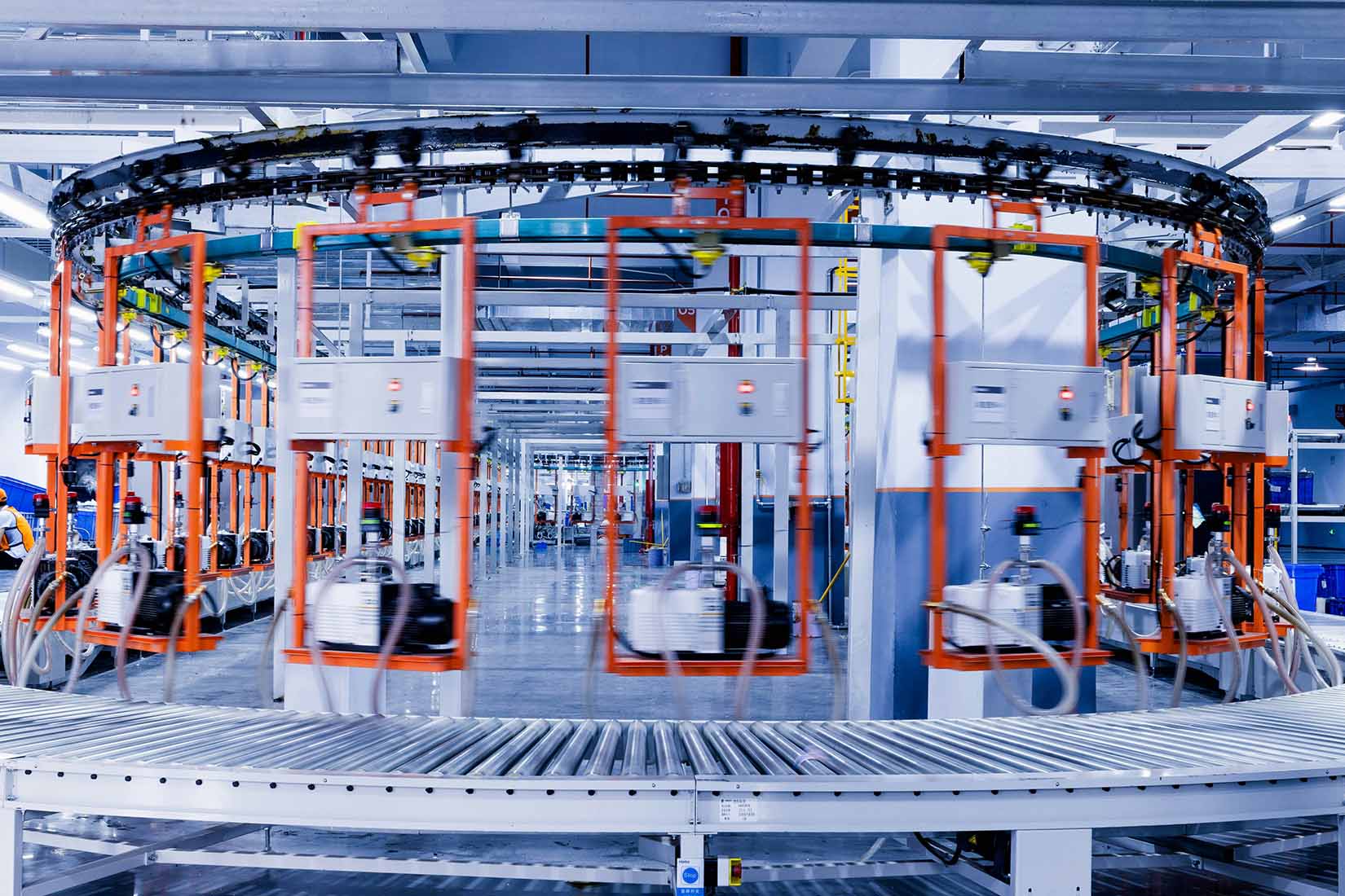 A modern industrial facility features a circular conveyor system with multiple automated stations and bright overhead lighting.