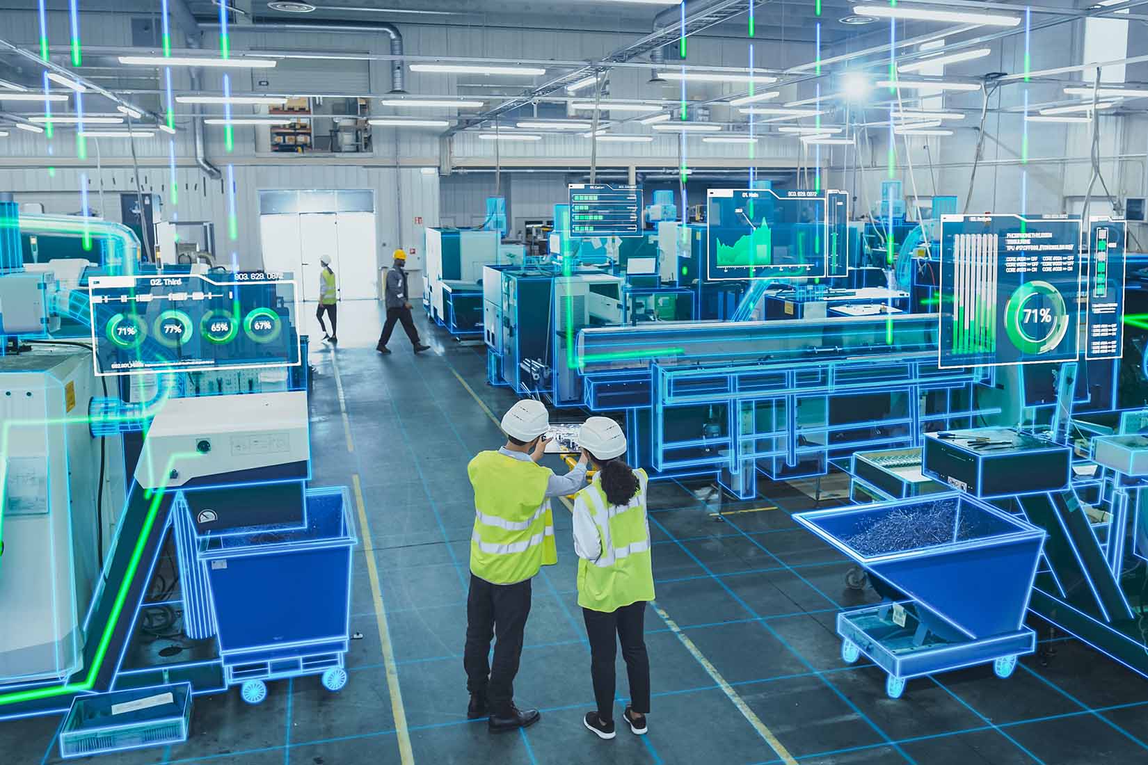 In a modern factory, two individuals review performance metrics on screens while surrounded by advanced production equipment.