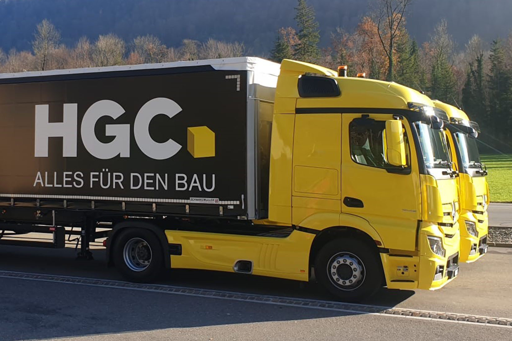 Three bright yellow trucks are parked side by side, showcasing a large black trailer with the HGC logo prominently displayed.