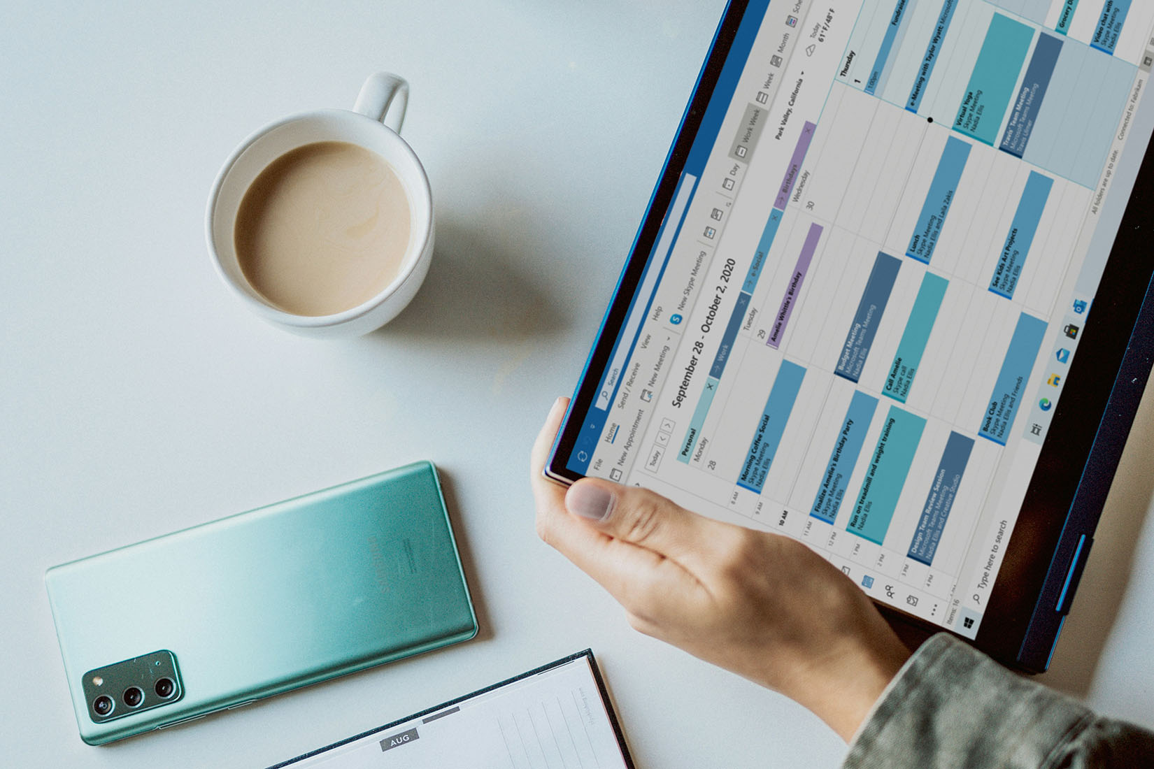 A steaming cup of coffee is positioned next to a laptop screen filled with a vibrant calendar, indicating a busy week ahead.