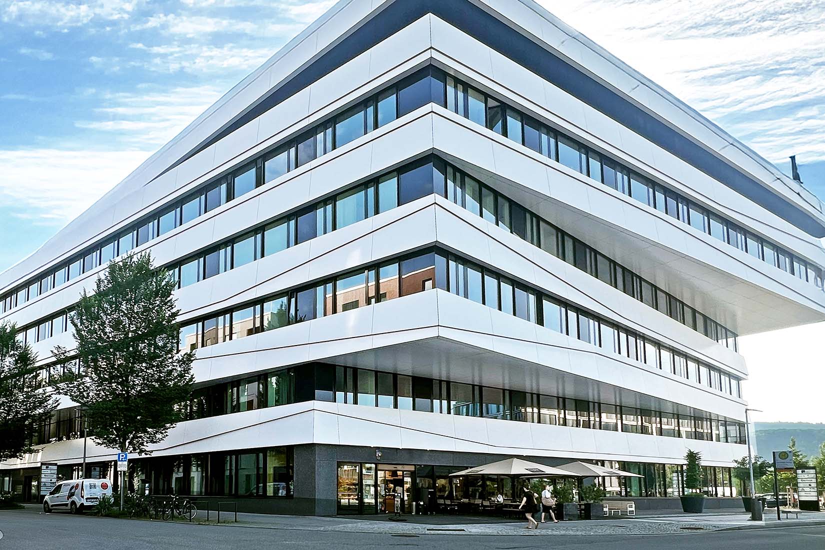 A modern building of io with a sleek, angular design features large windows and a shaded outdoor seating area.