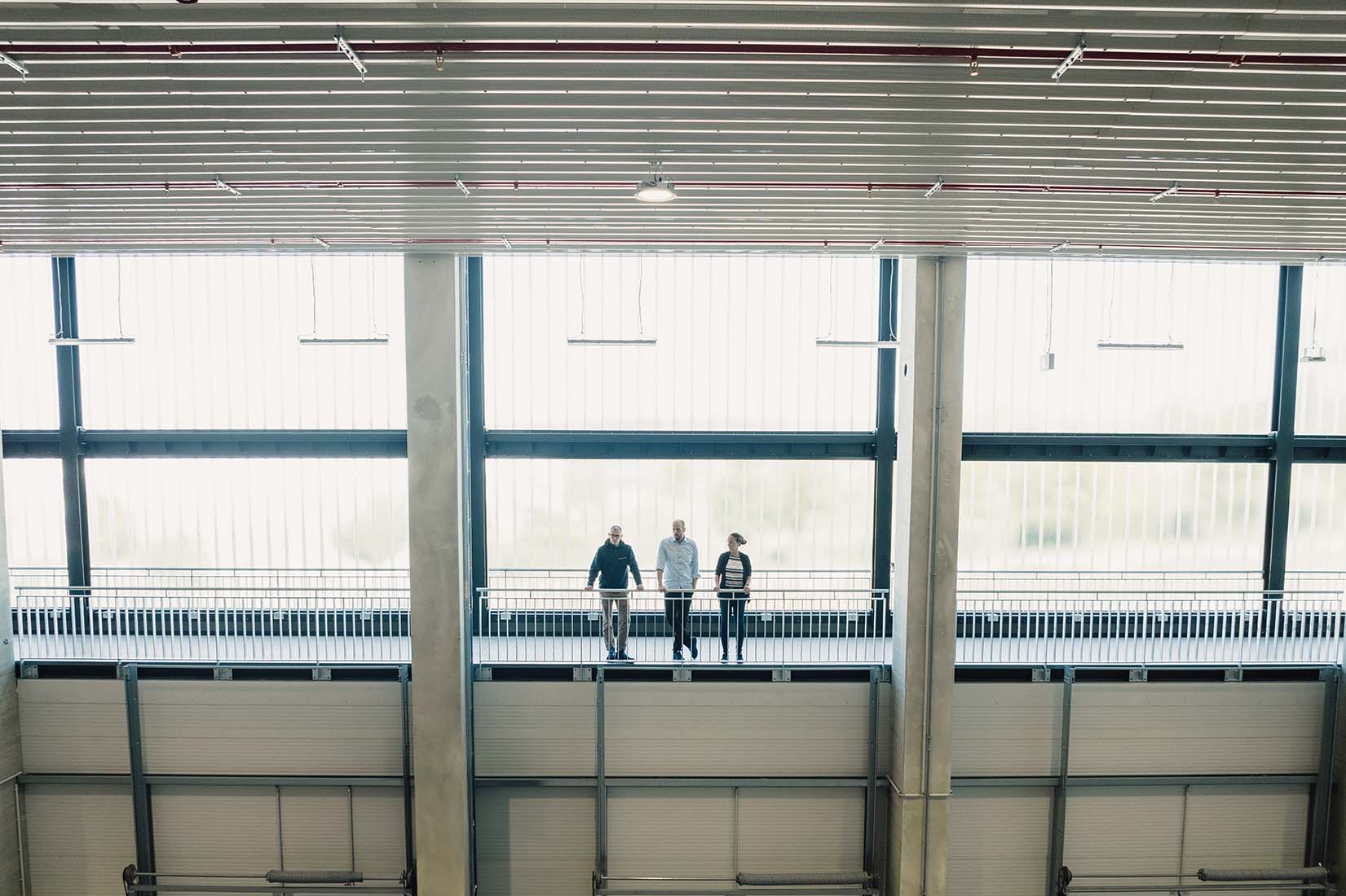 Three people are standing on the skywalk inside the hall