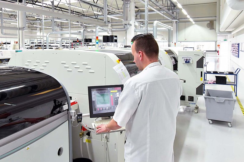 In einer hellen Fabrikhalle steuert ein Mitarbeiter eine Maschine, um den Produktionsprozess zu überwachen.