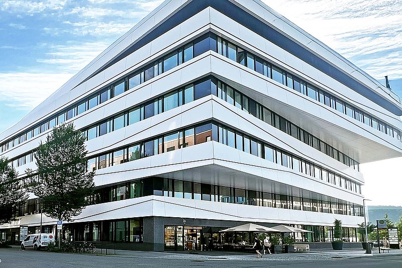 Das Bürogebäude von io hat eine auffällige, moderne Architektur und ist von einer grünen Umgebung mit Bäumen und Pflanzen umgeben.