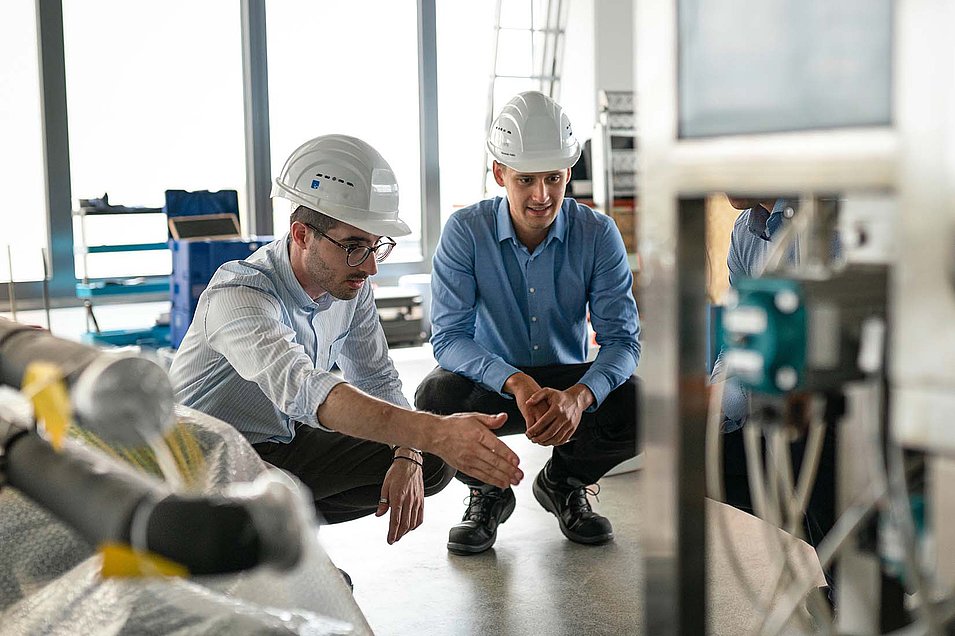 Two men wearing construction helmets discuss a problem on site