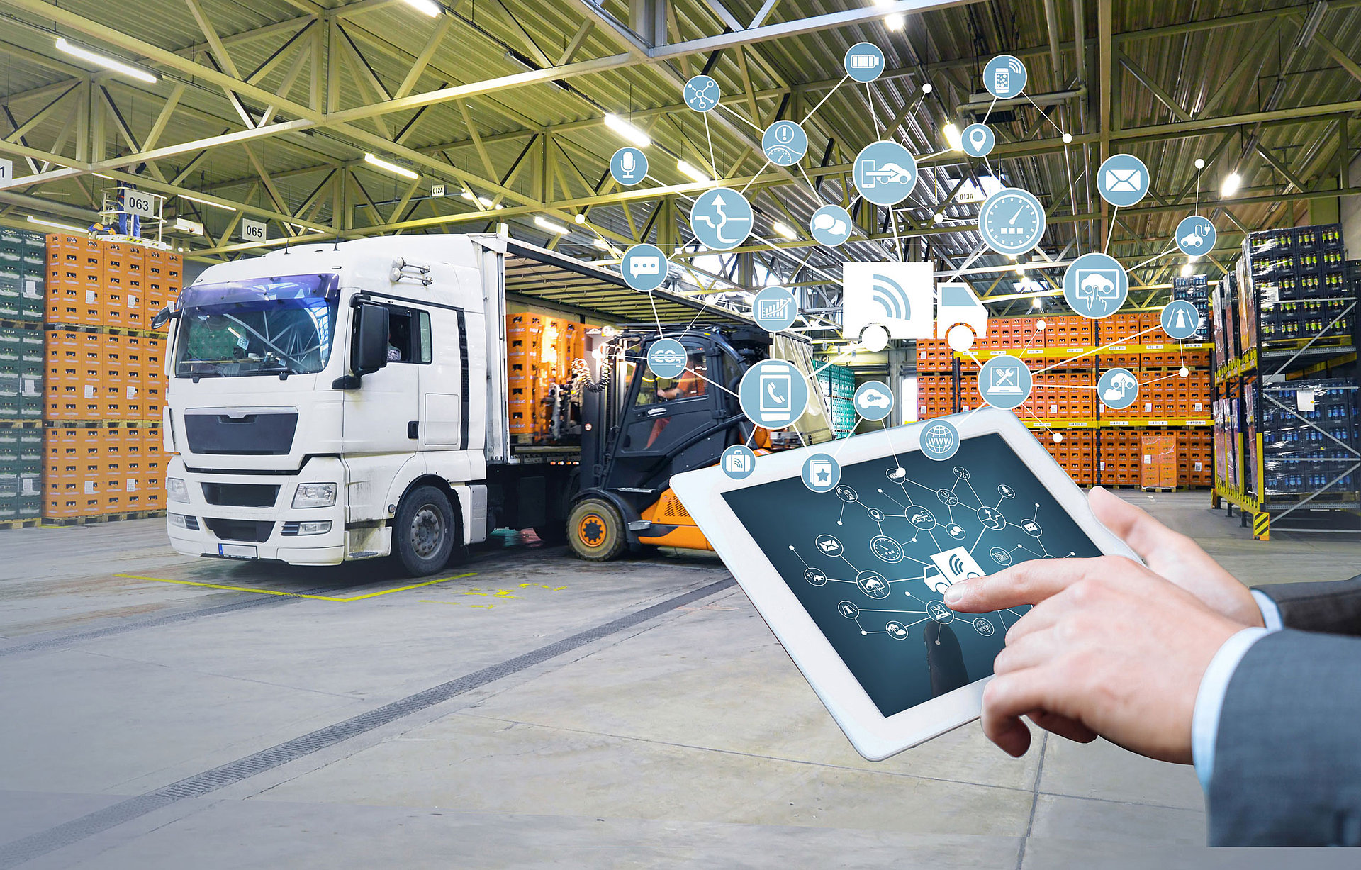 A finger points to a tablet with connected symbols and in the background, a truck is loaded with boxes