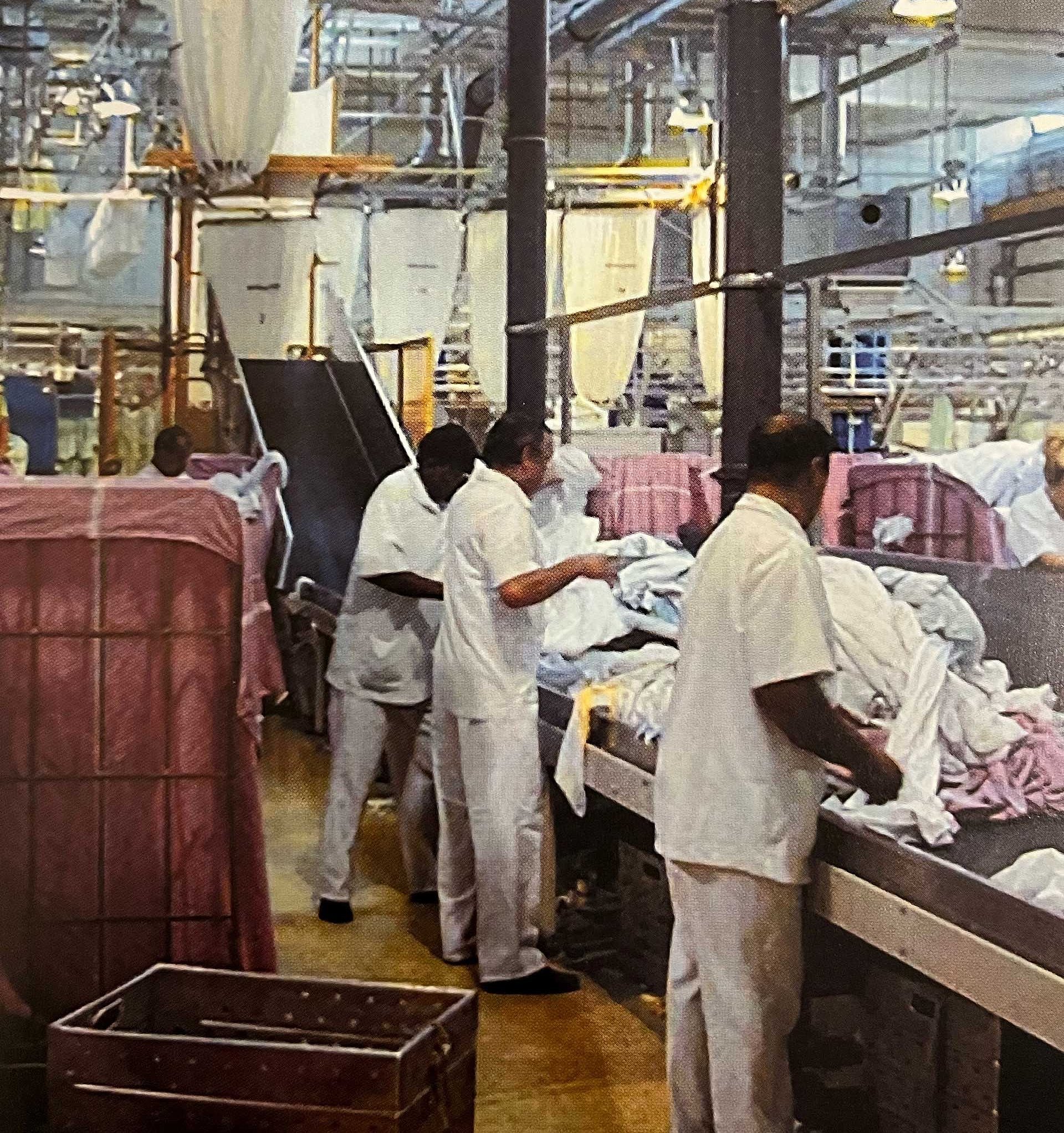 Mitarbeiter einer Großwäscherei stehen am Fließband und sortieren Laken