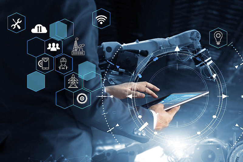 In einem modernen Umfeld nutzt ein Mann ein Tablet, umgeben von Symbolen für Technologie und Industrie, während ein Roboterarm arbeitet.