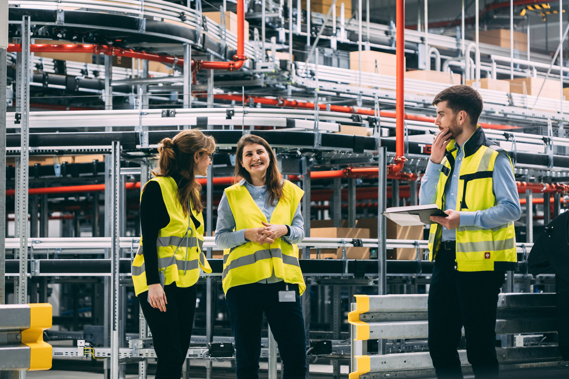 Consultants stand in front of conveyor belts in the logistics hall